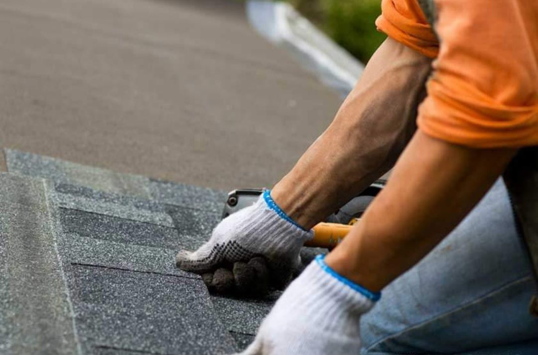 A man wearing gloves is working on a roof.