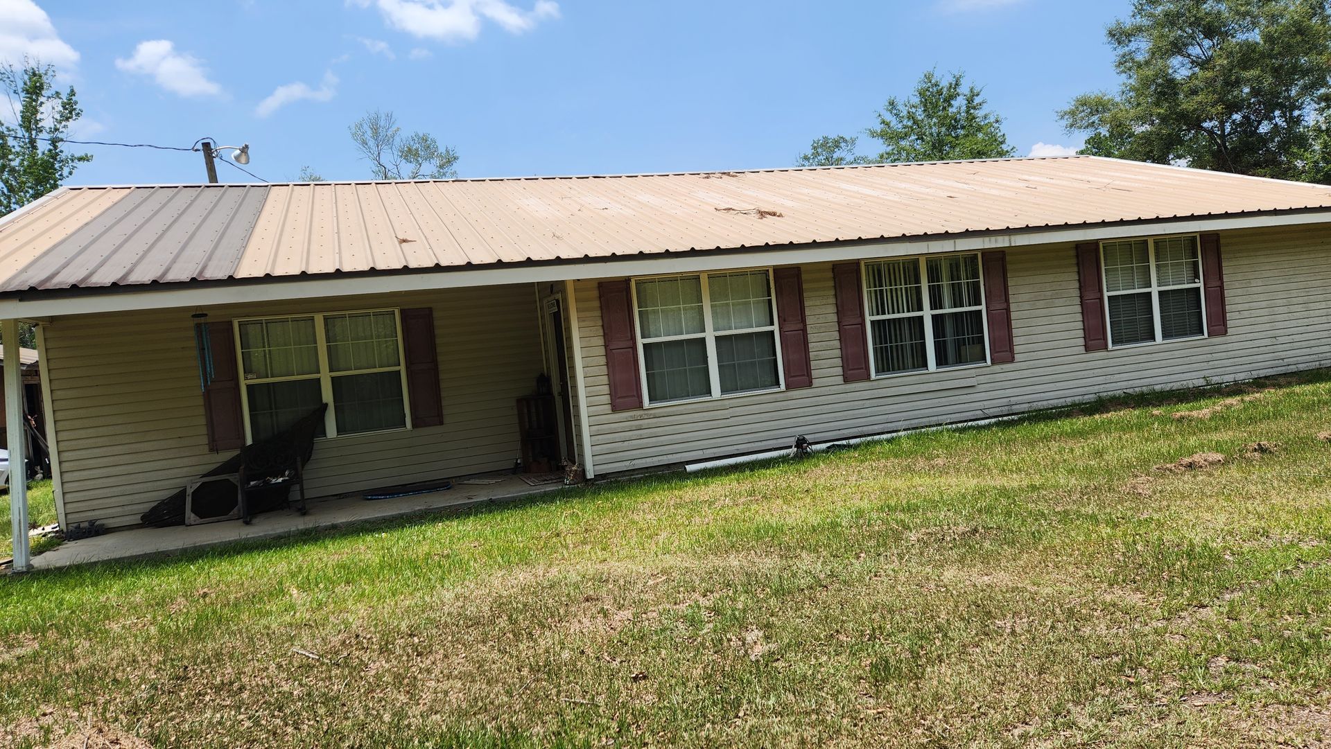 A white house with a metal roof and red shutters is sitting on top of a lush green field.