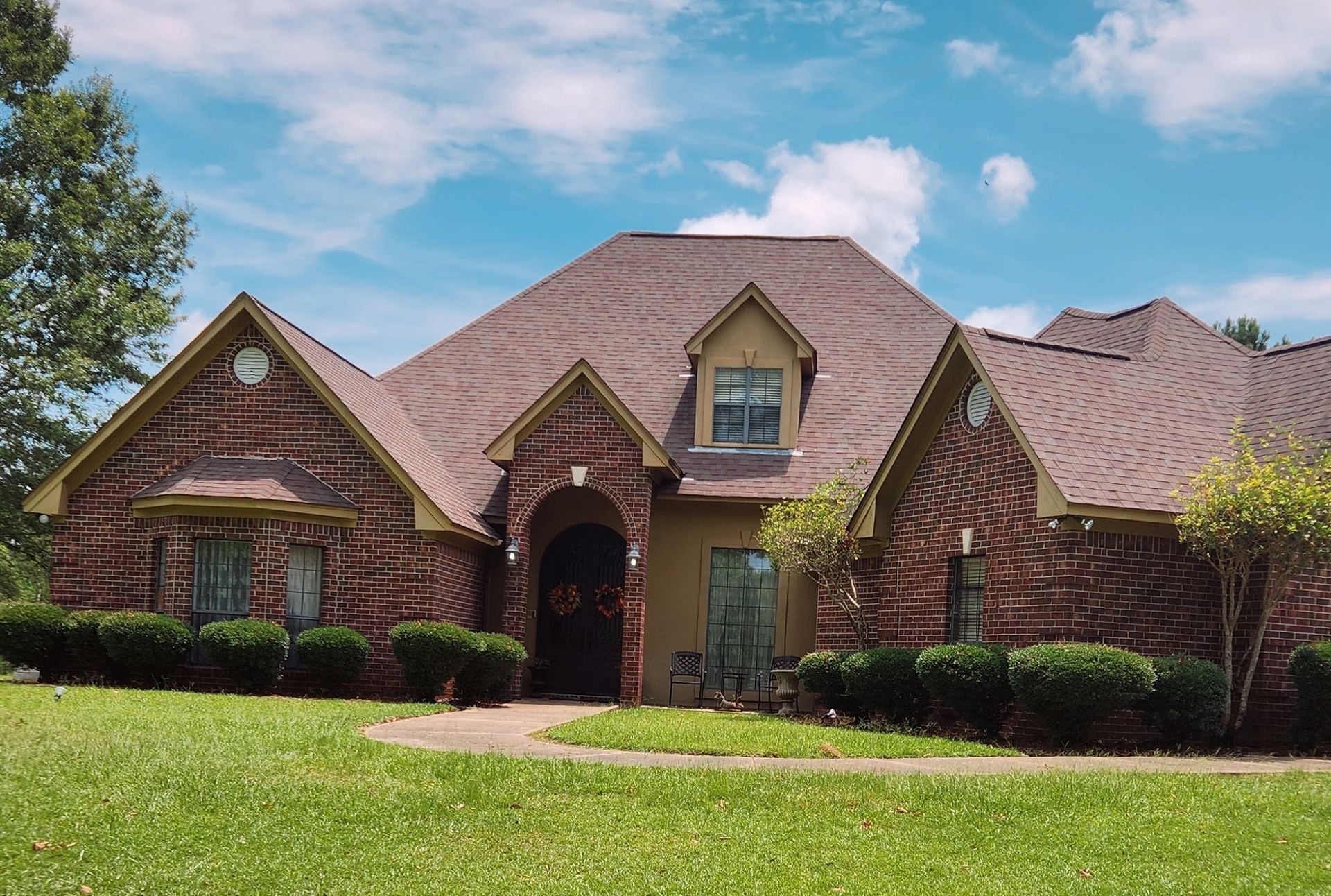 A large brick house with a brown roof is sitting on top of a lush green lawn.