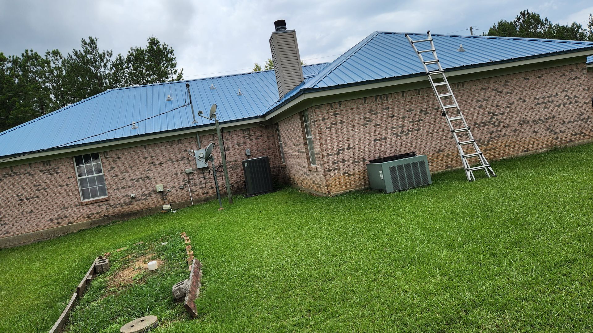 A brick house with a blue roof and a ladder in the backyard.
