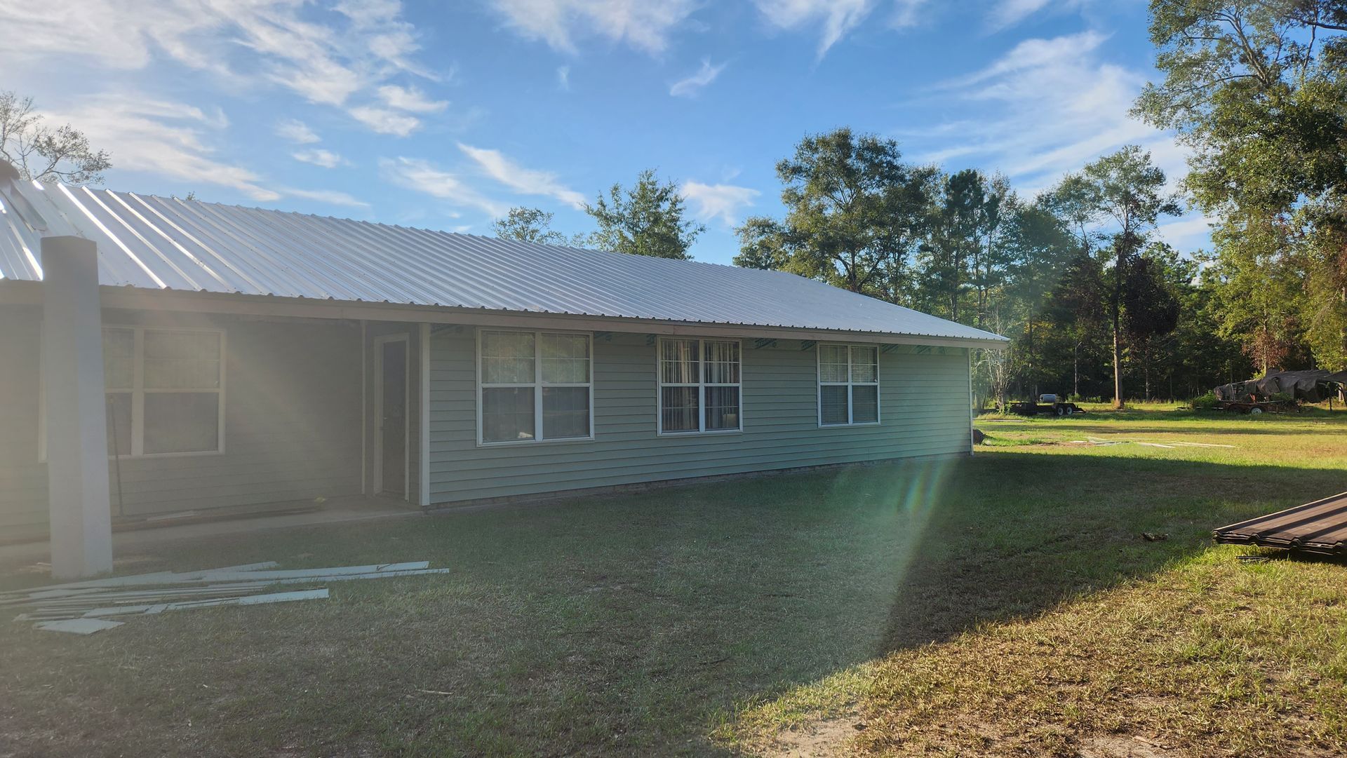 A white house with a metal roof is sitting on top of a lush green field.