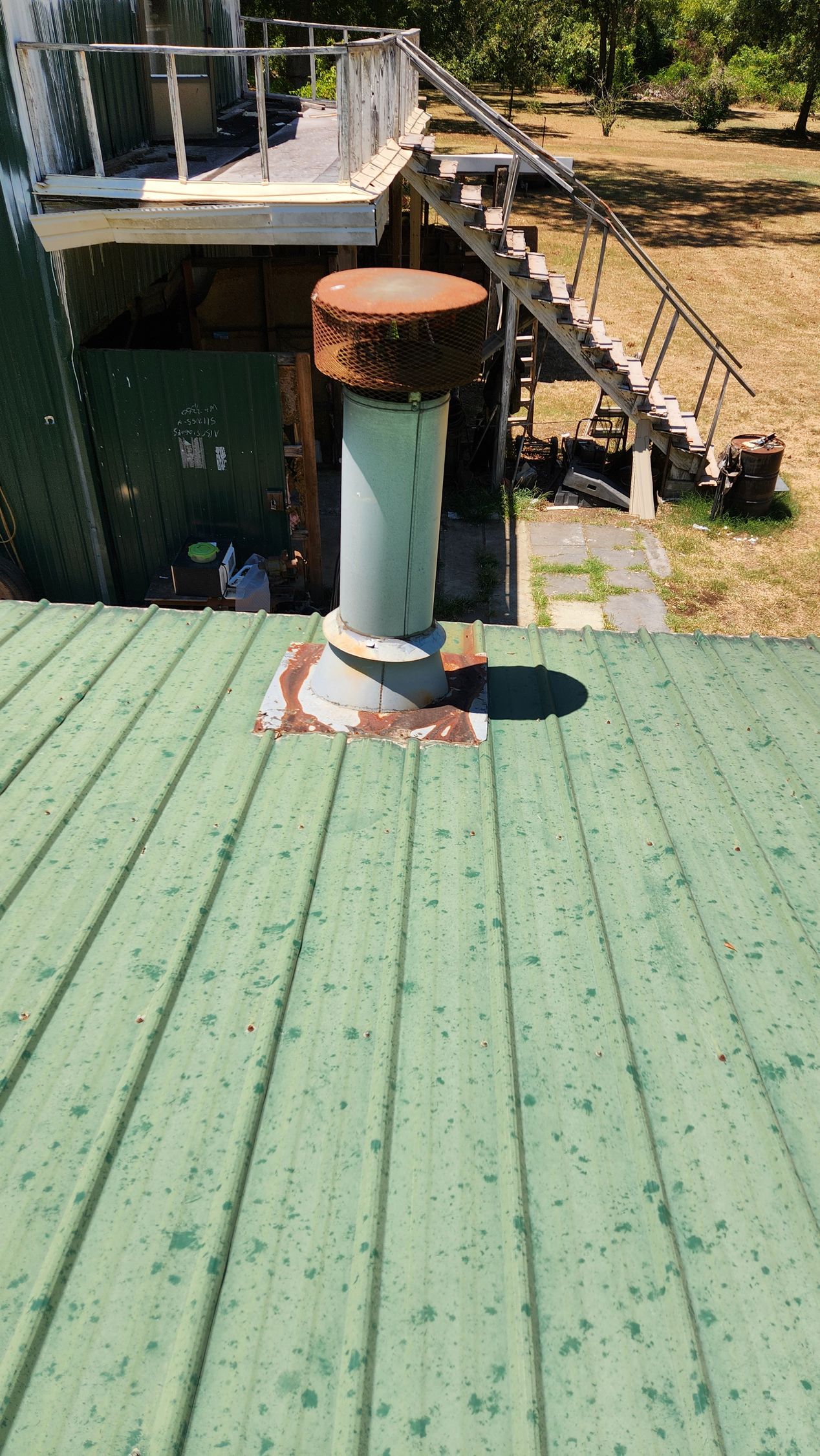 A green roof with a rusty chimney on top of it.