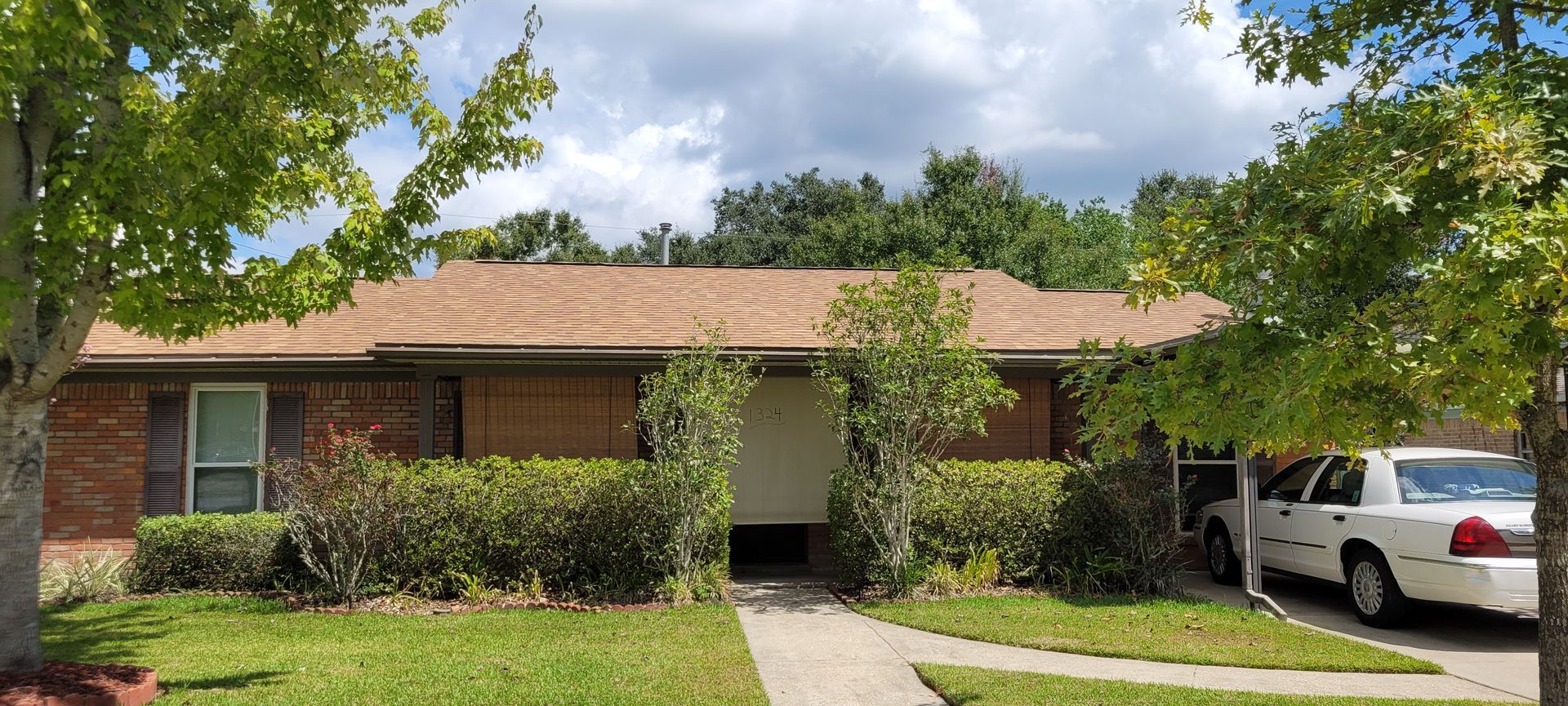 A white car is parked in front of a brick house.