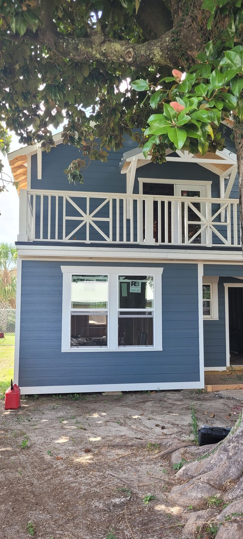 A blue house with a balcony and a tree in the background.