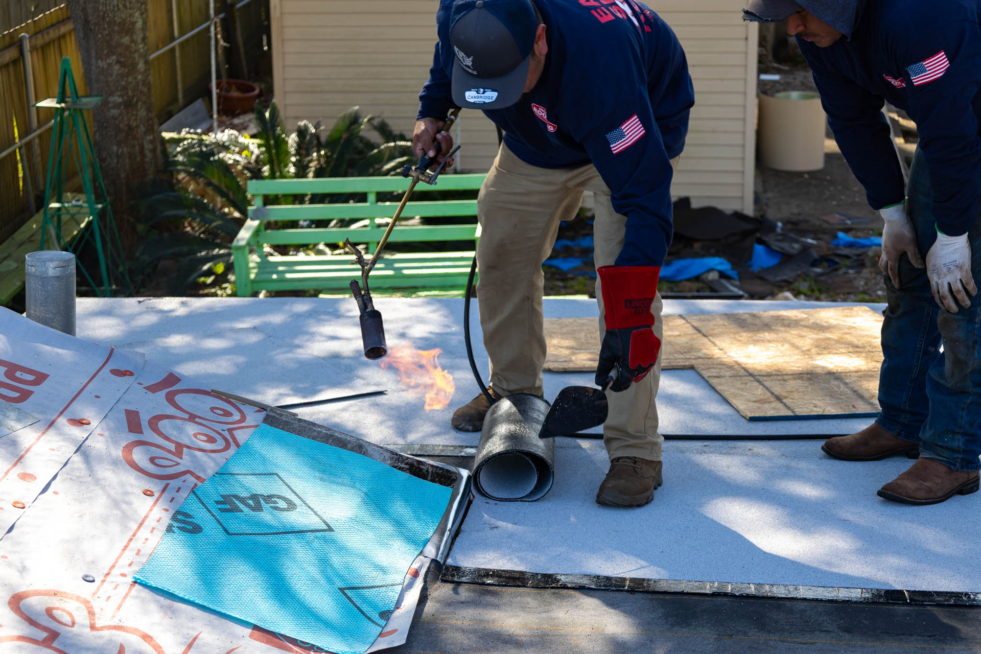 Two men are working on a roof with a torch.
