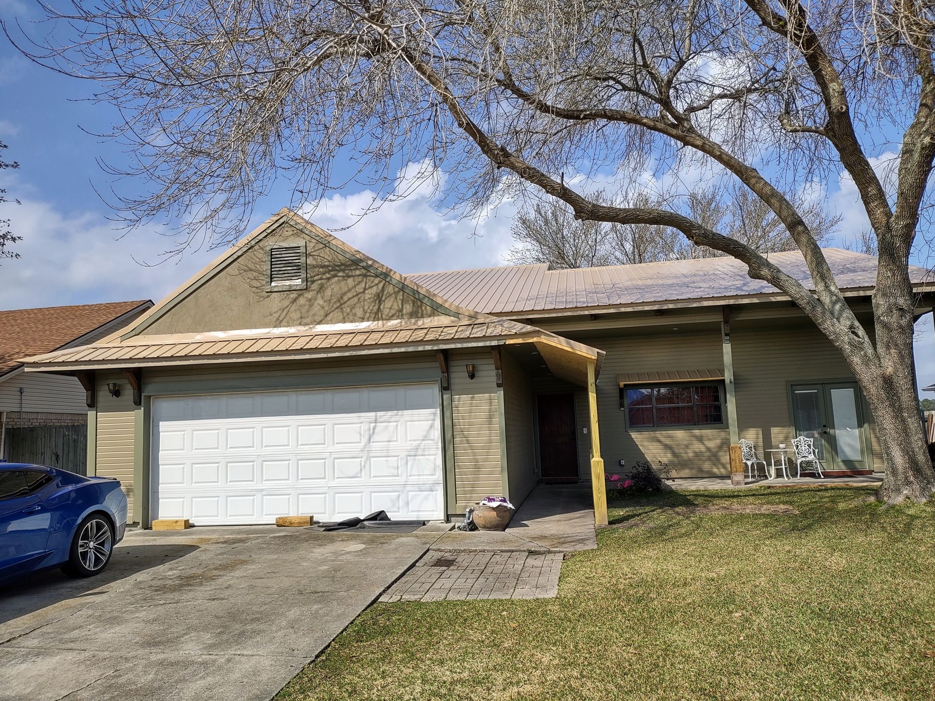 A blue car is parked in front of a house with a garage door.