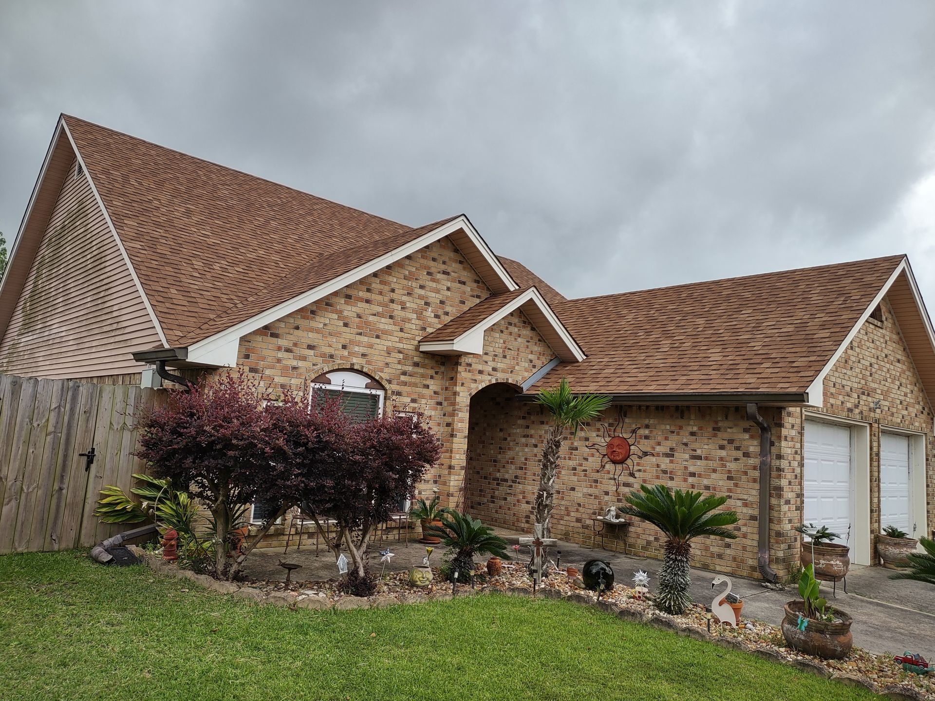 A brick house with a brown roof and a fence in front of it.