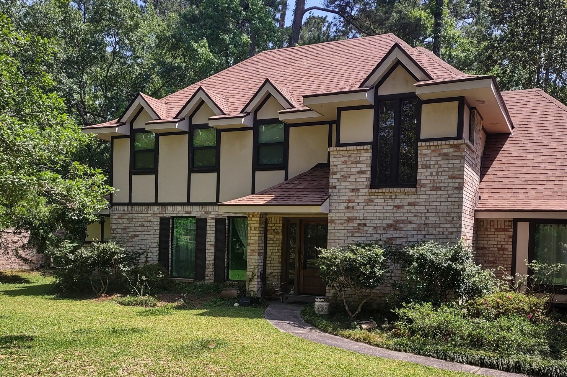 A large brick house with a red roof is surrounded by trees