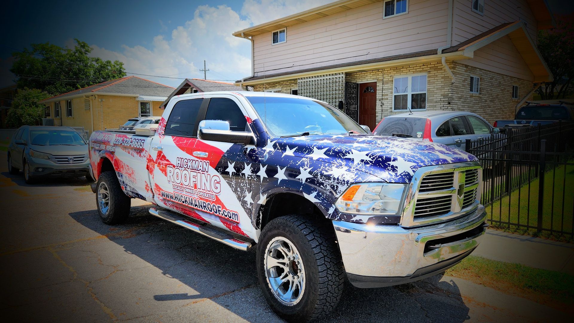 A truck with the american flag wrapped around it is parked in front of a house.