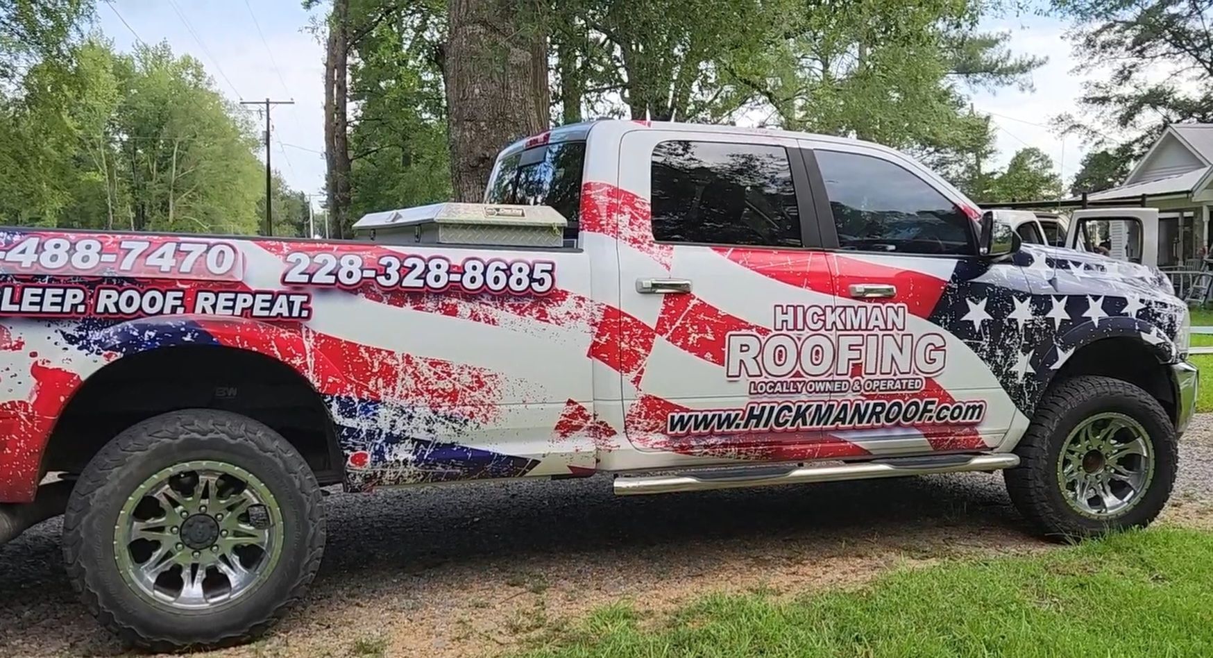 A red , white and blue roofing truck is parked in front of a house.