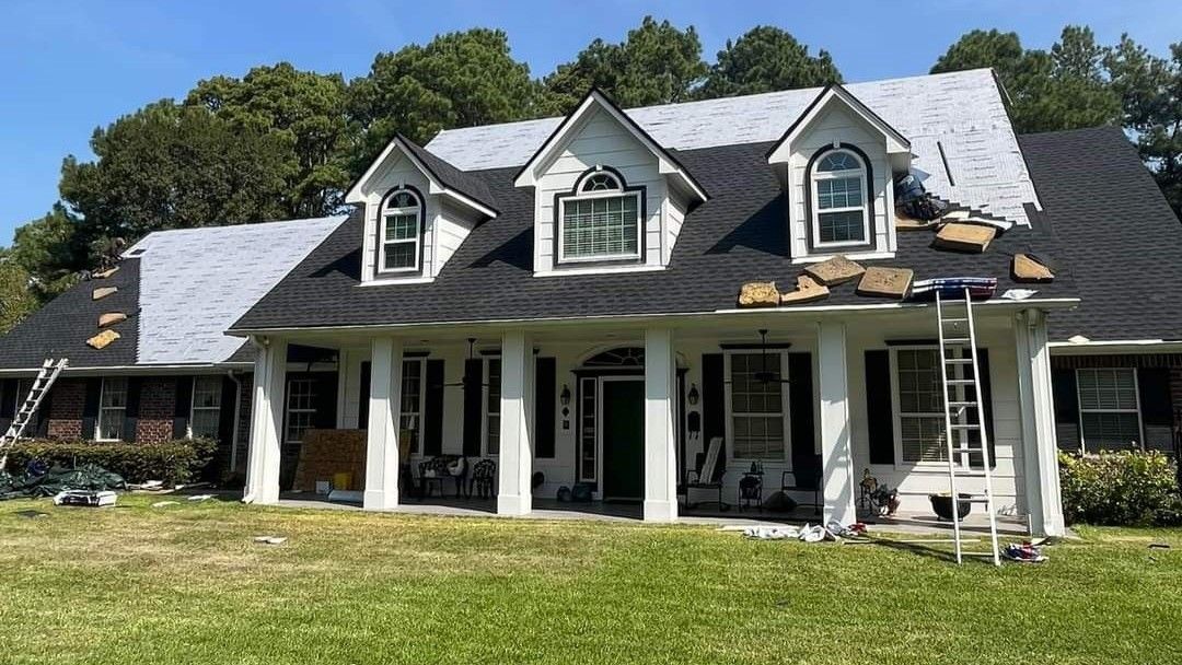 A large white house with a black roof is being remodeled.