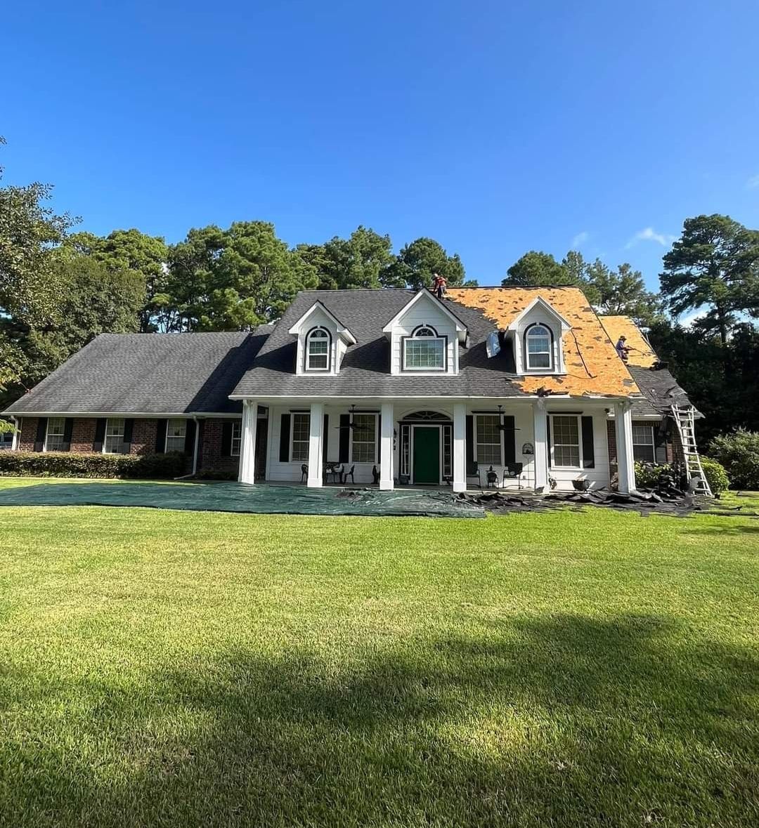 A large white house with a gray roof is sitting on top of a lush green field.