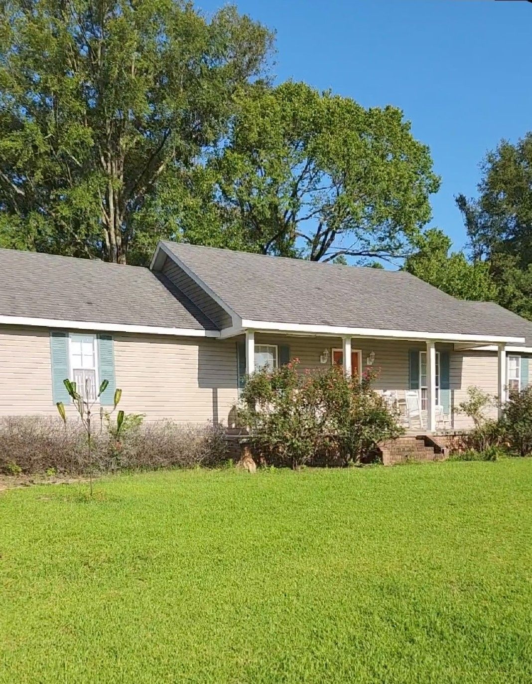 A house with a gray roof sits in the middle of a lush green field.