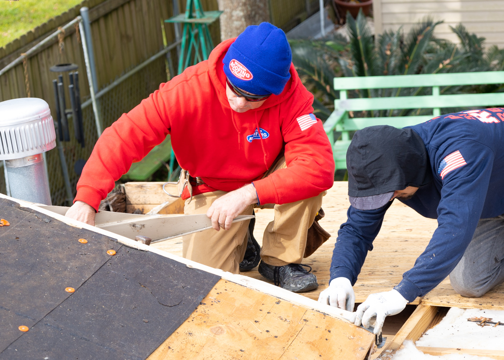Two men are working on a roof with a saw.