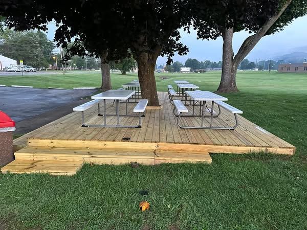 A wooden deck with picnic tables under a tree