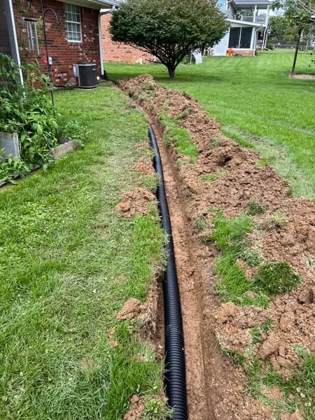 A drain pipe is being installed in a yard next to a house.