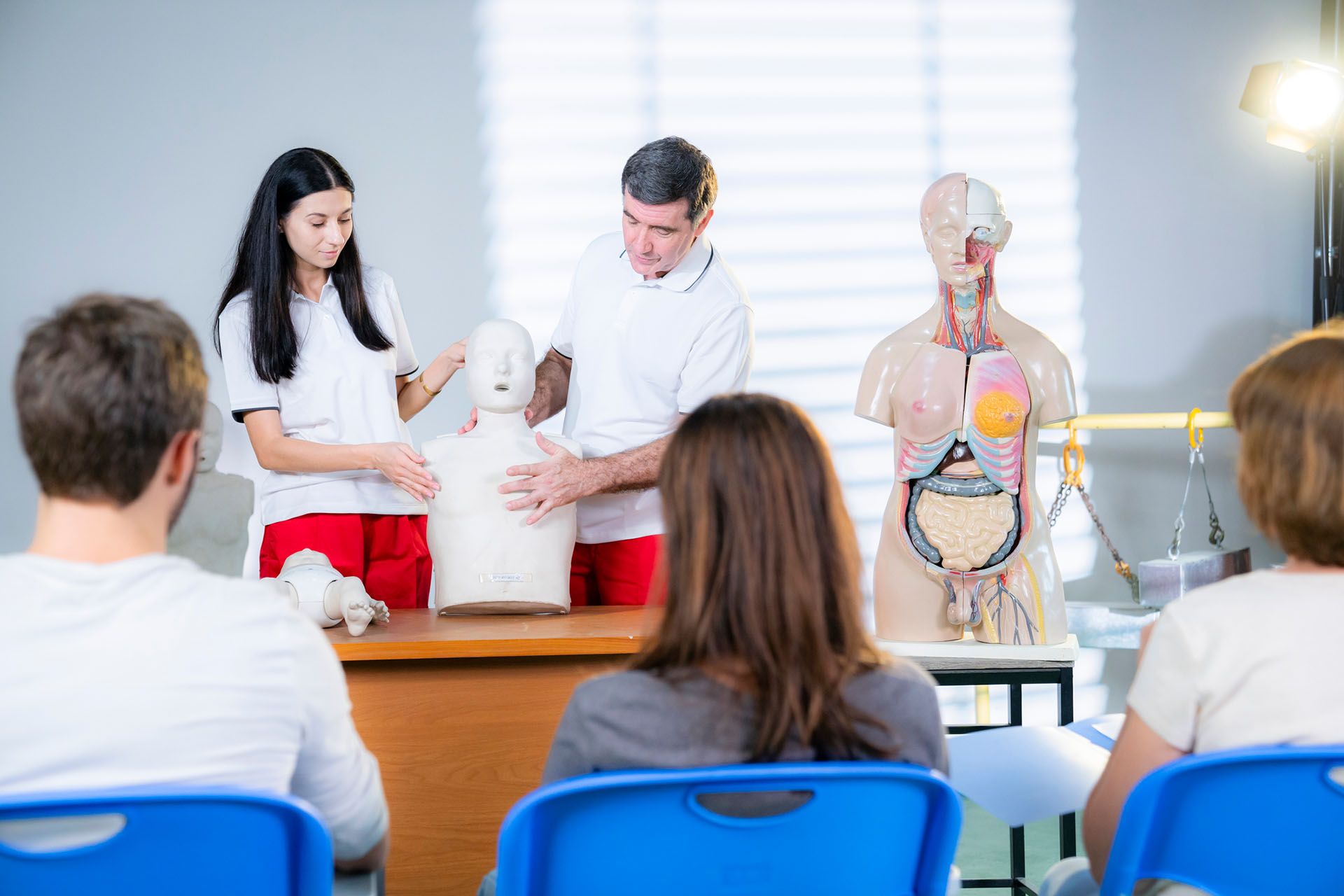 A group of people is sitting in front of a mannequin in a classroom