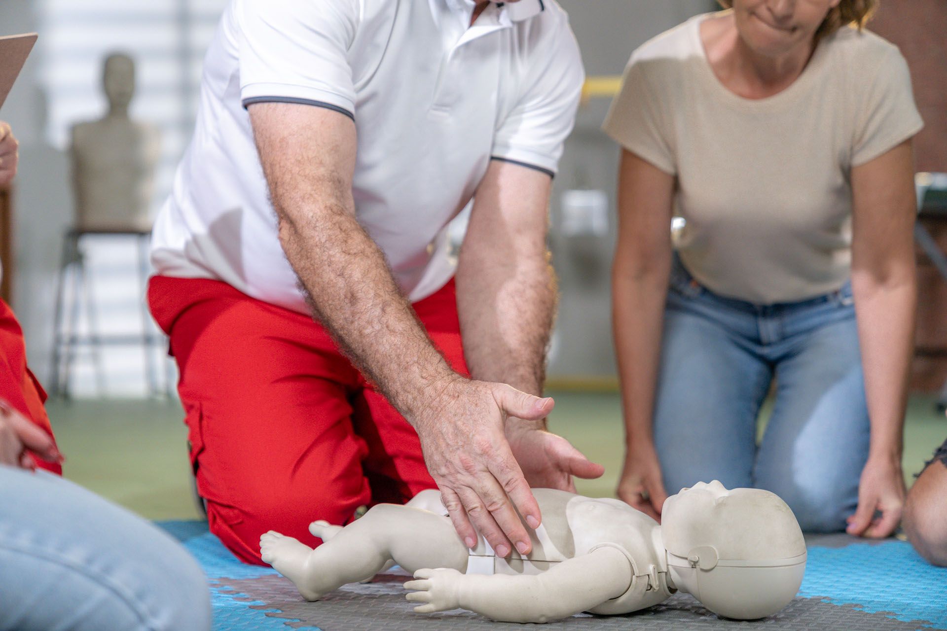 A man is kneeling next to a baby mannequin