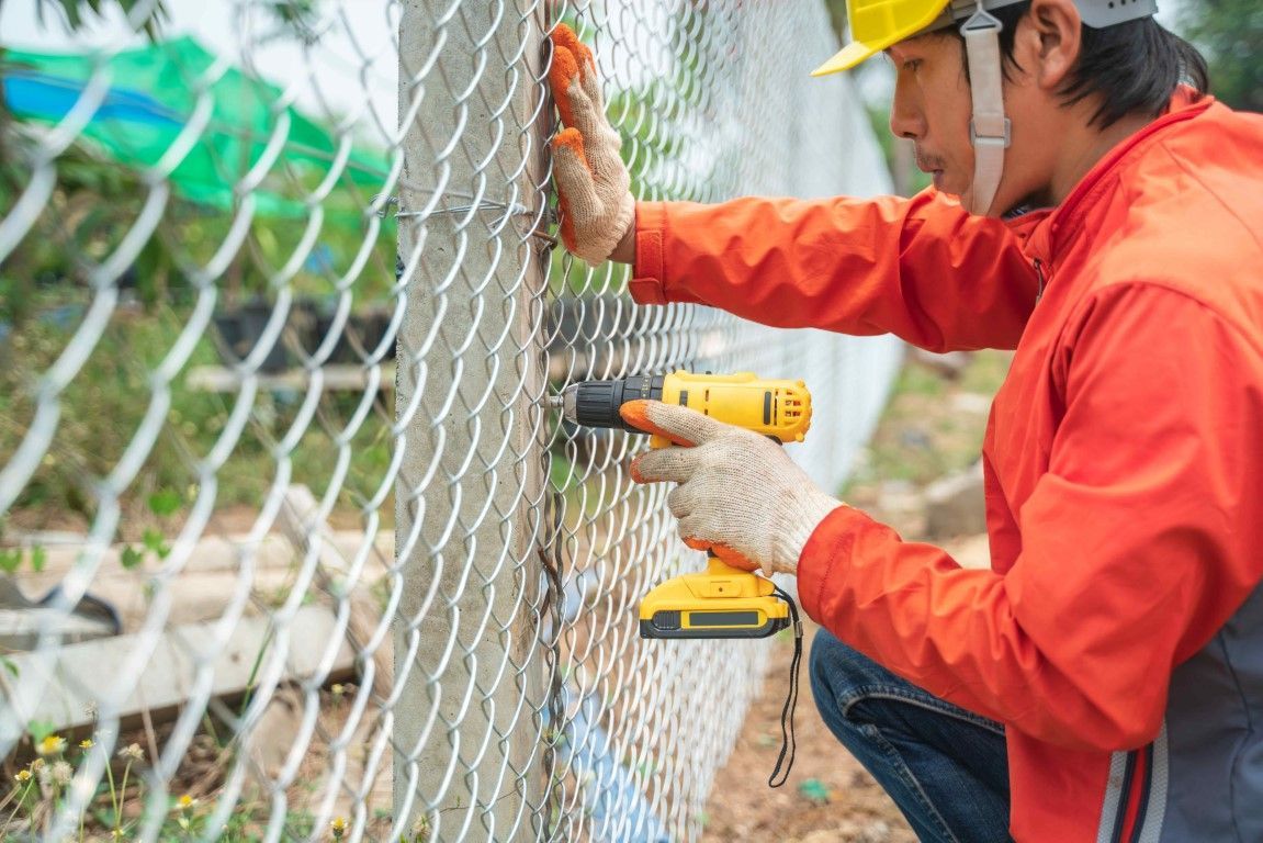 Man in orange jacket and green hat installing wire fence outdoors in winter.