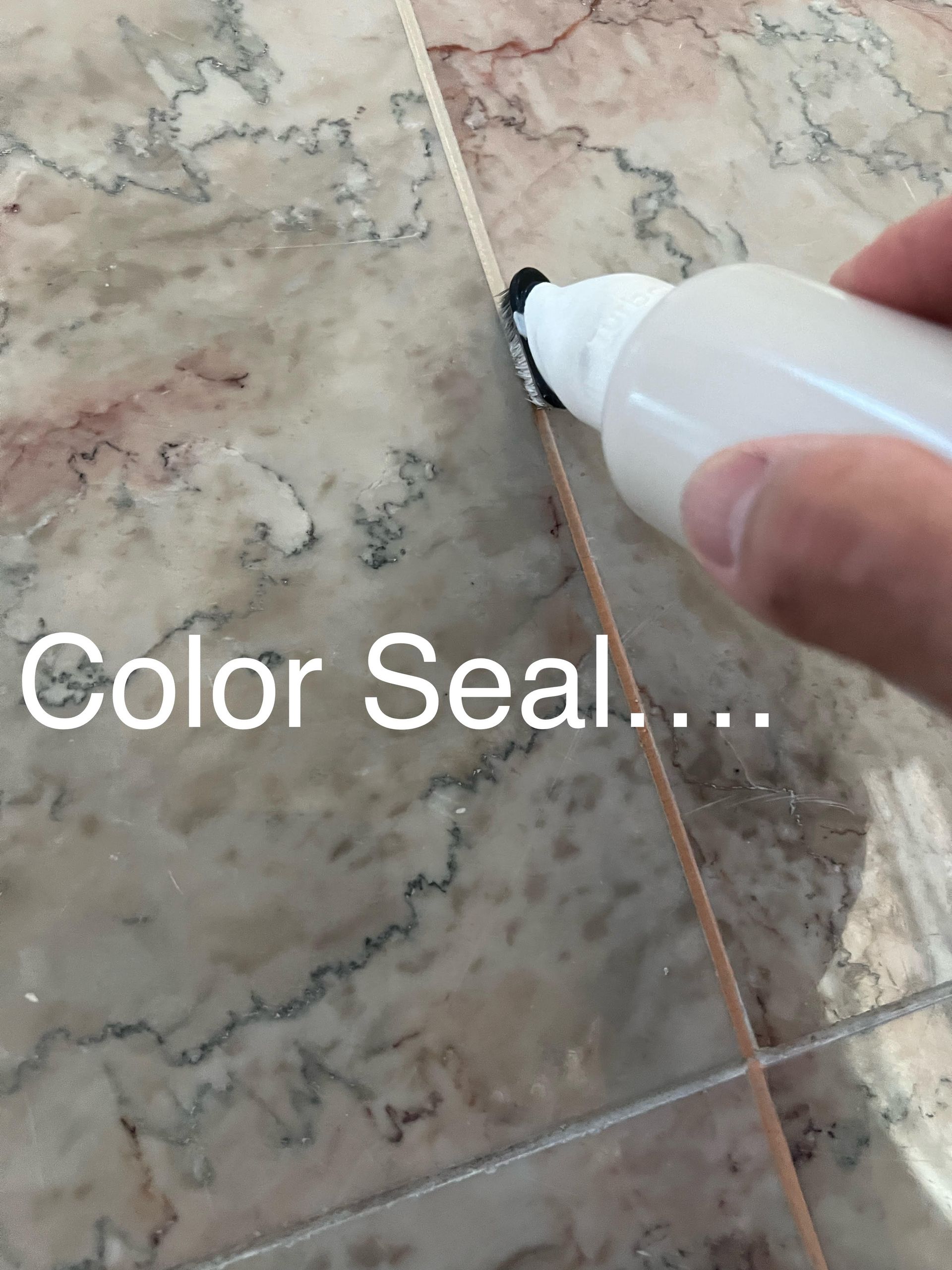 Hand using a color seal applicator on a grout line between marble tiles.