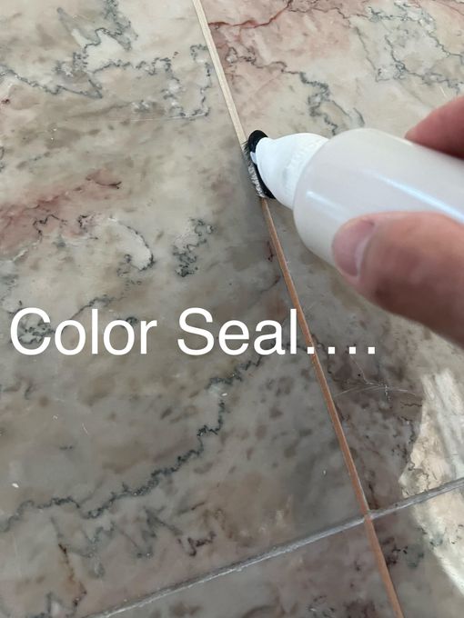 Hand using a color seal applicator on a grout line between marble tiles.