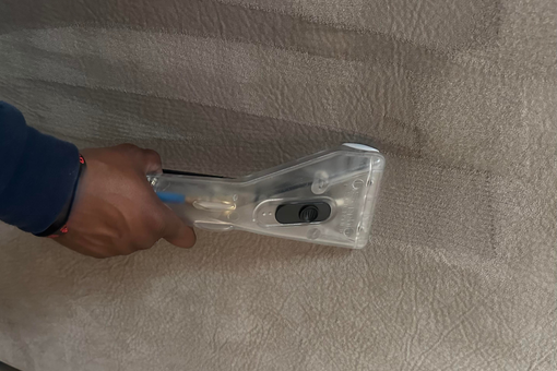 Person cleaning a tan couch with a handheld upholstery cleaning tool.