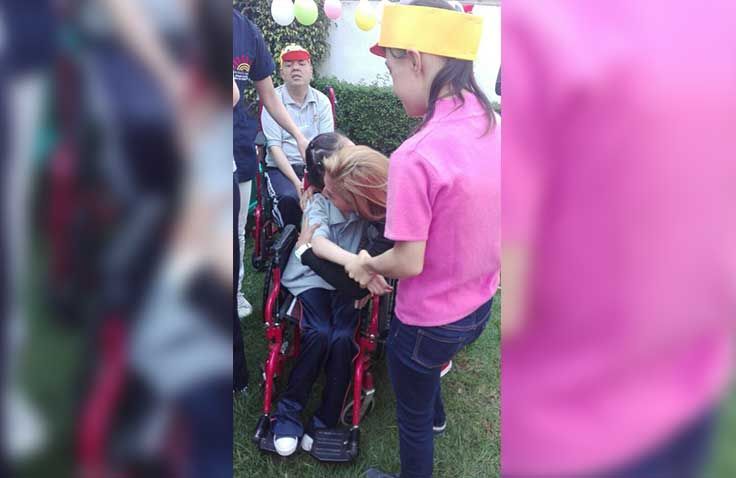 Una mujer con una camisa rosa está ayudando a un hombre en silla de ruedas.