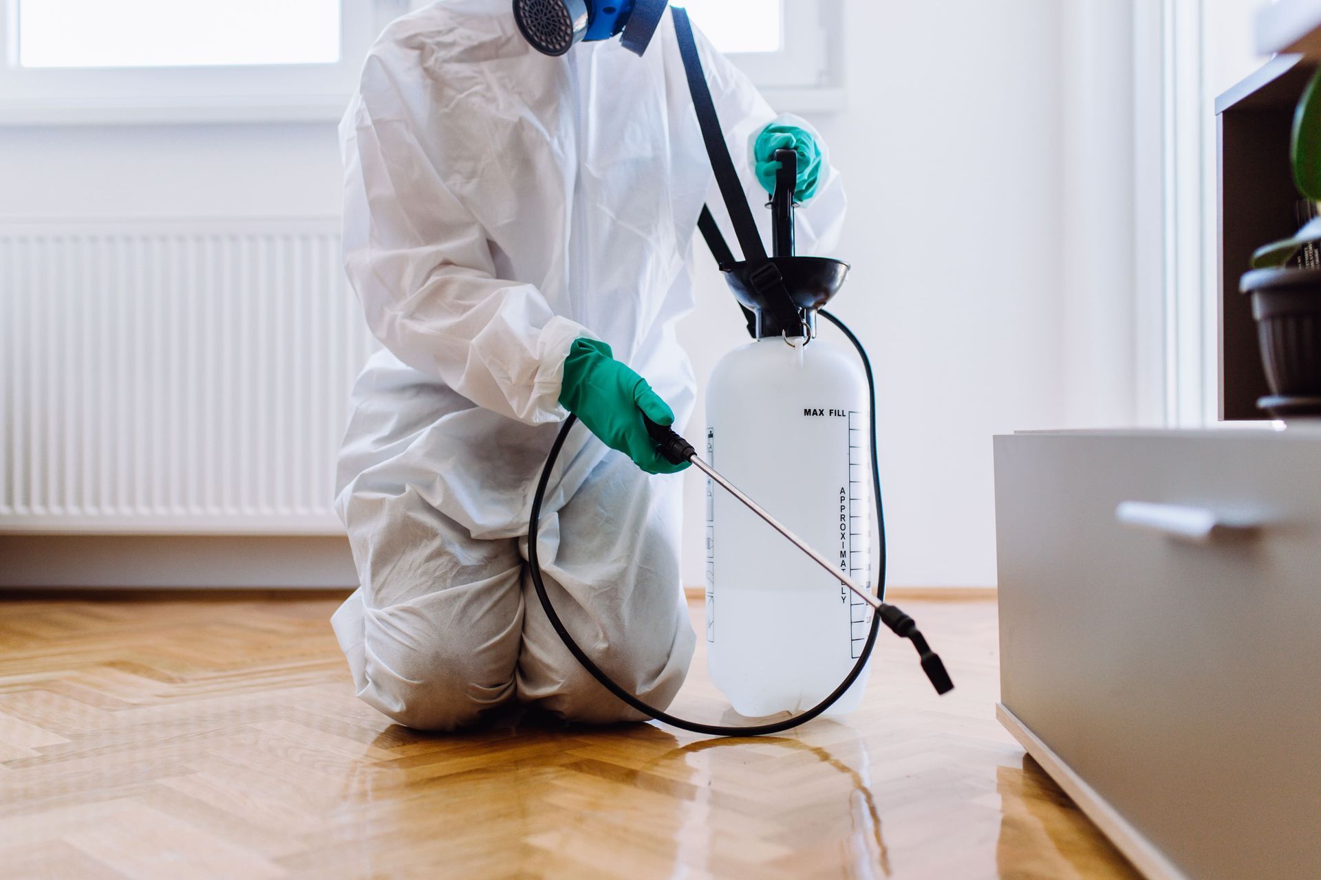 Person in protective suit spraying floor with insecticide.