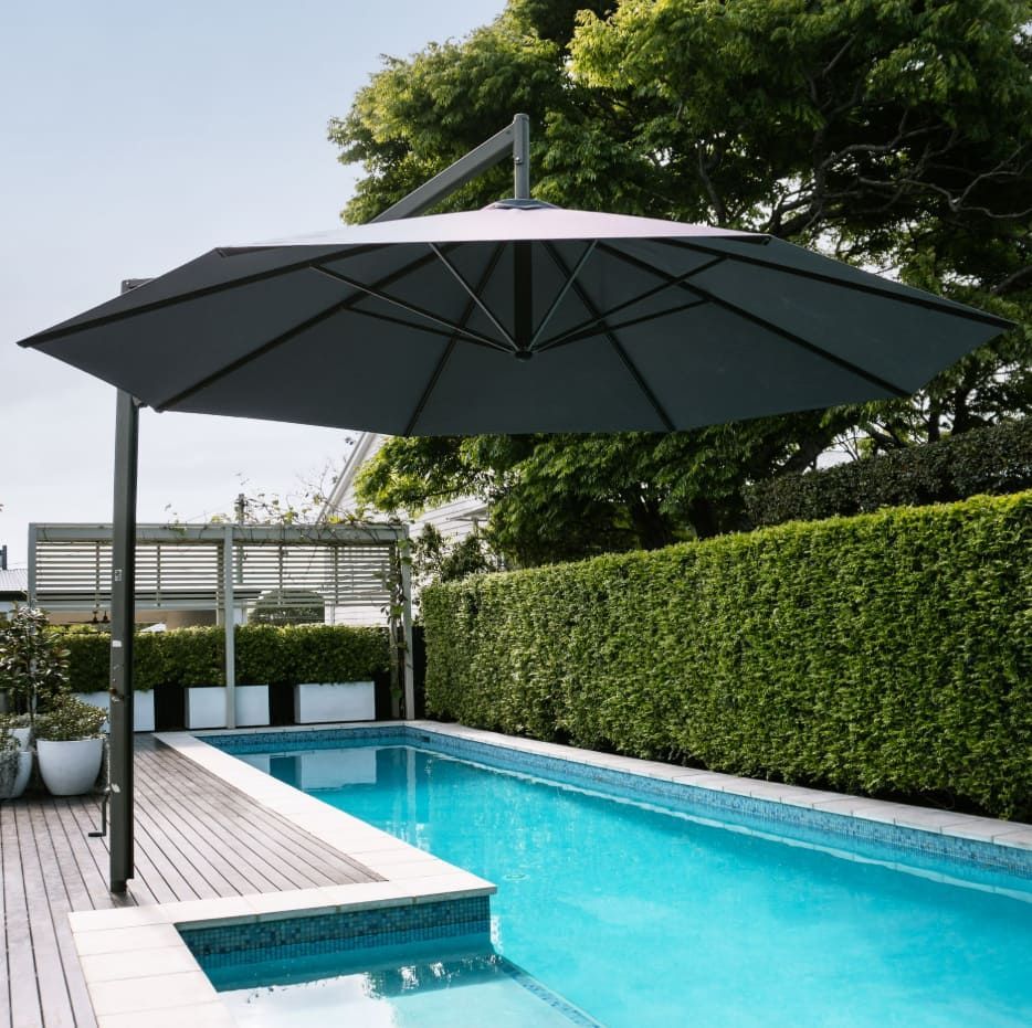 A Large Umbrella Sits Over A Swimming Pool — Coastal Blind Installations In Kensington, QLD