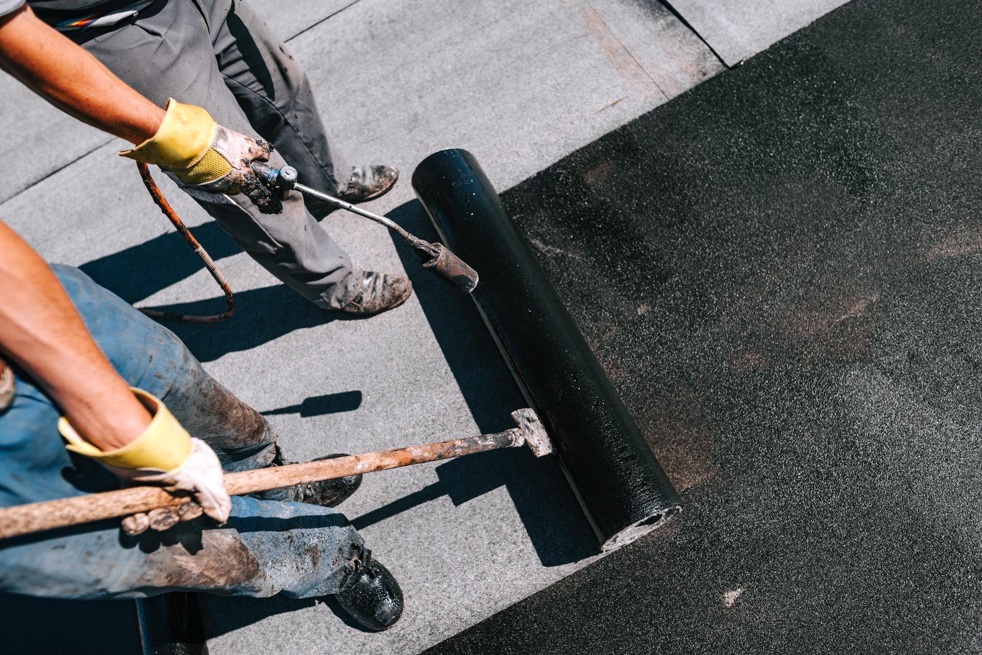Roofing crew performing flat roof repair by rolling out a new membrane on a commercial low-slope roof. Roofing crew performing flat roof repair by rolling out a new membrane on a commercial low-slope roof.