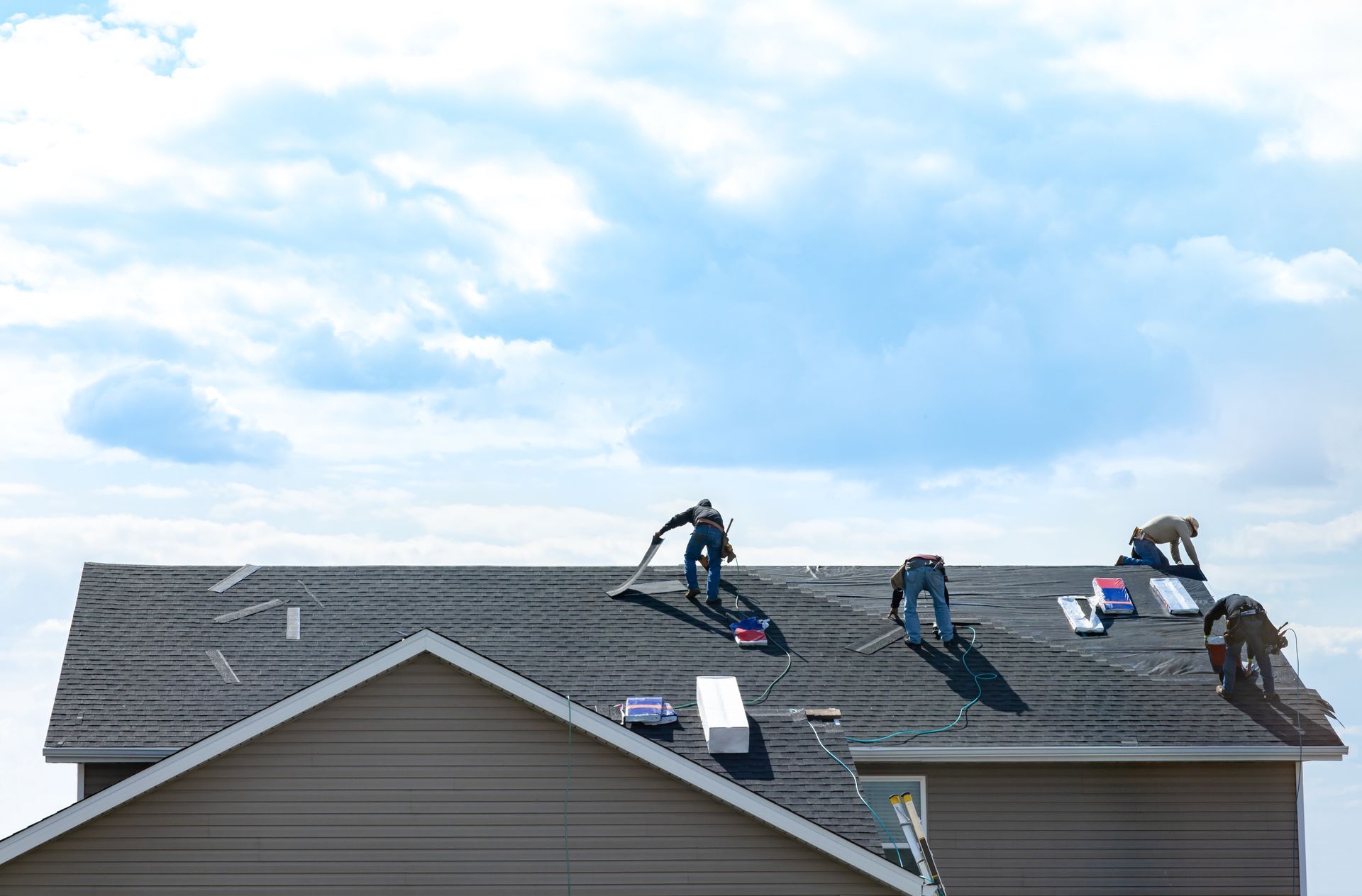 Workers installing shingles on a residential rooftop under a blue sky. Workers installing shingles on a residential rooftop under a blue sky.