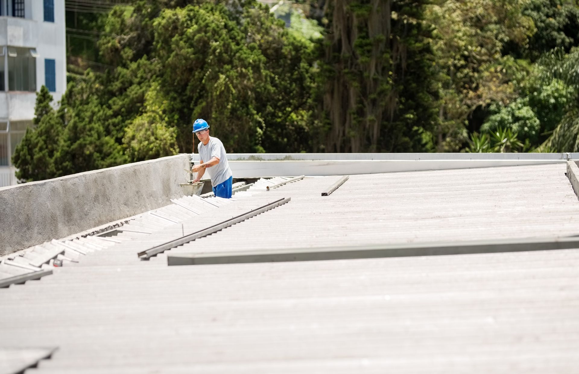 A man installing materials on a commercial flat roofing, focused on his work under a clear blue sky.