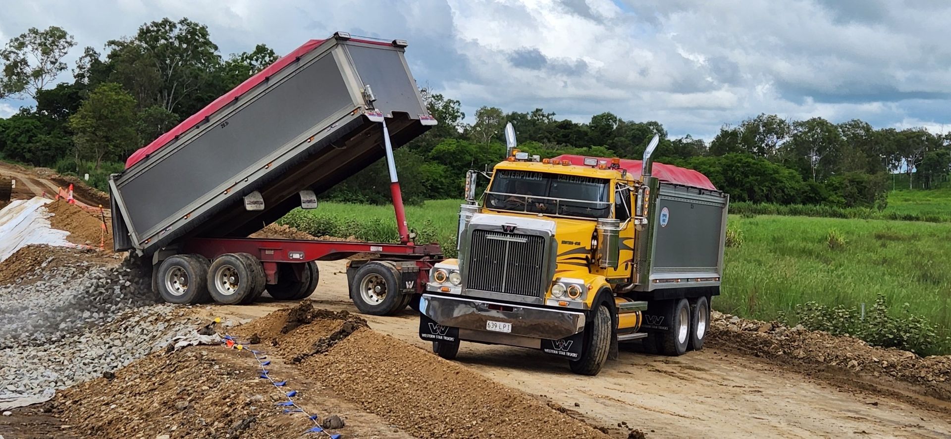 A Yellow Dump Truck Is Driving Down A Dirt Road — Petersen Tippers in Farleigh, QLD