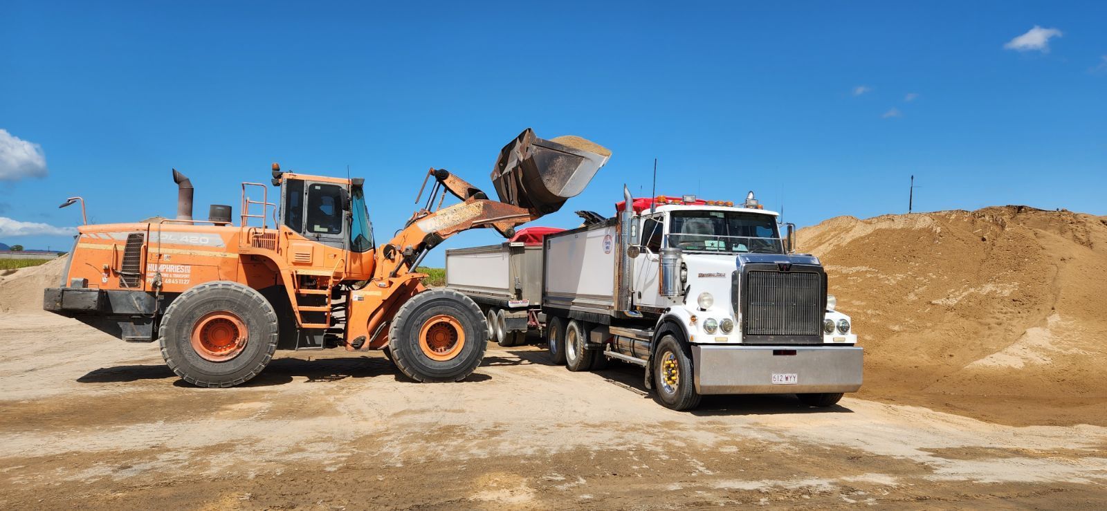 A Bulldozer Is Loading Dirt Into A Dump Truck — Petersen Tippers in Farleigh, QLD