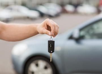Hand holding car keys in front of a blue car.