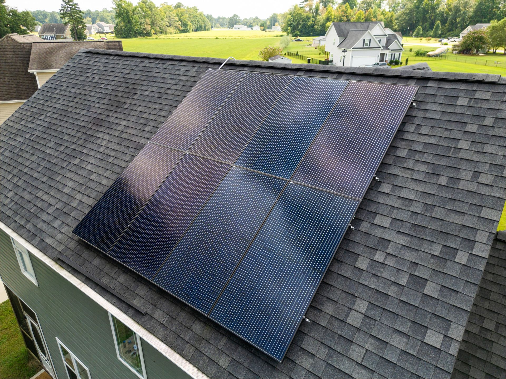 Solar panels installed on a dark gray shingled roof of a house.