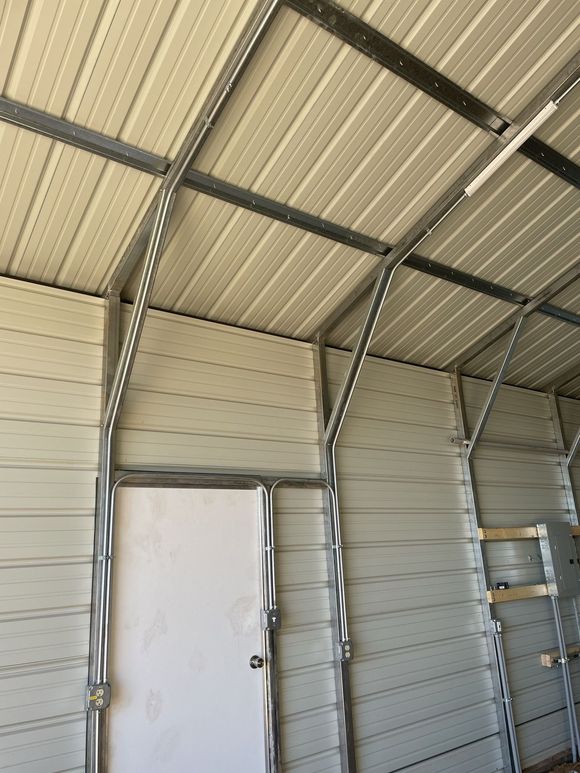 Interior of a metal building with a white door and metal framing. Beige metal siding and roof.