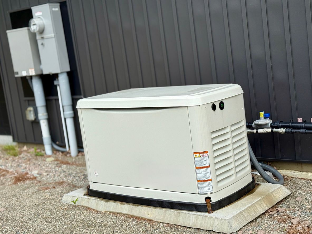 A beige standby generator outside a dark building, connected to electrical boxes.