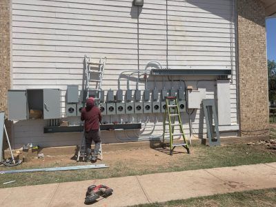 Construction worker installing electrical meters on a building exterior. Green ladder and materials are present.