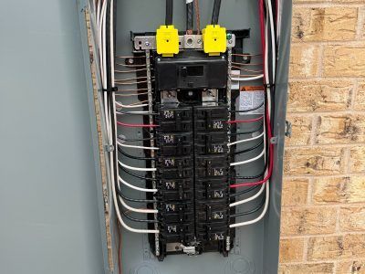 Electrical panel with black circuit breakers, copper and white wires. Yellow covers on top. Mounted on brick.
