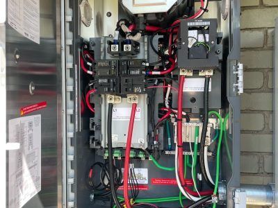 Open electrical panel with wires and circuit breakers. Red, black, and green wires are visible.
