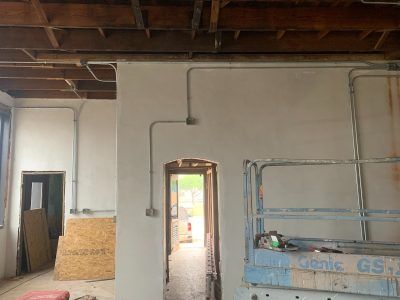 Interior view of a building under construction, showing electrical conduit on a white wall, doorway, and unfinished ceiling.