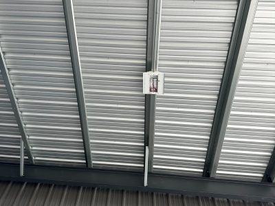 Metal corrugated roof with steel beams and a white electrical box.