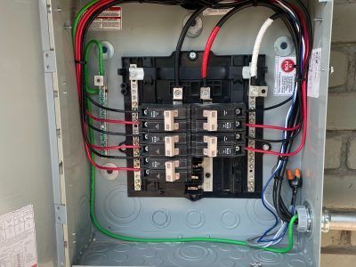Open electrical panel with black and white wires connected to breakers, green ground wires, and red power wires.