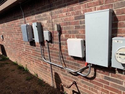 Electrical boxes and meter mounted on a brick wall, connected by conduit.