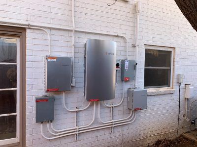 Solar power components mounted on a white brick exterior wall.