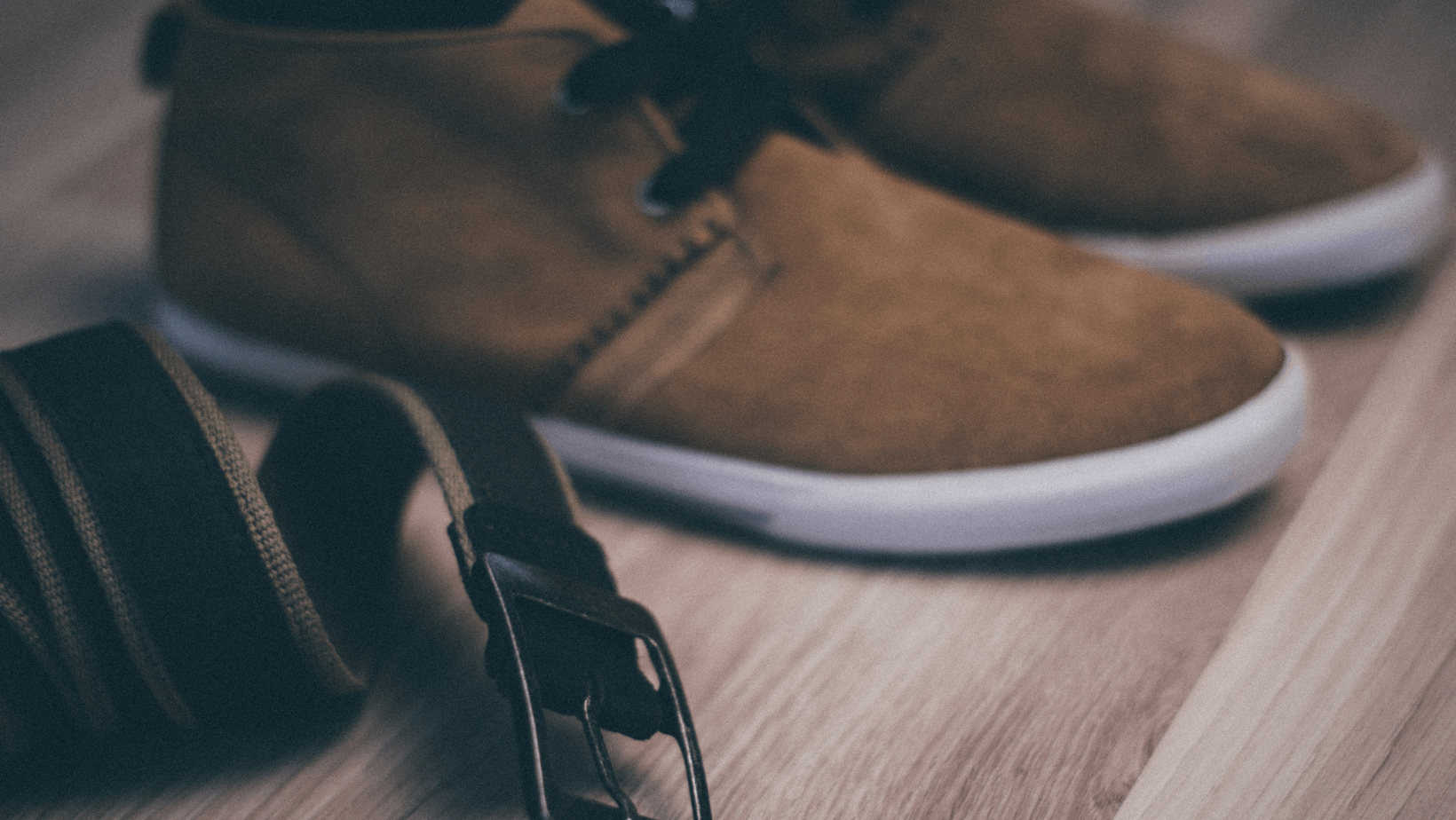 A pair of shoes and a belt are on a wooden floor.