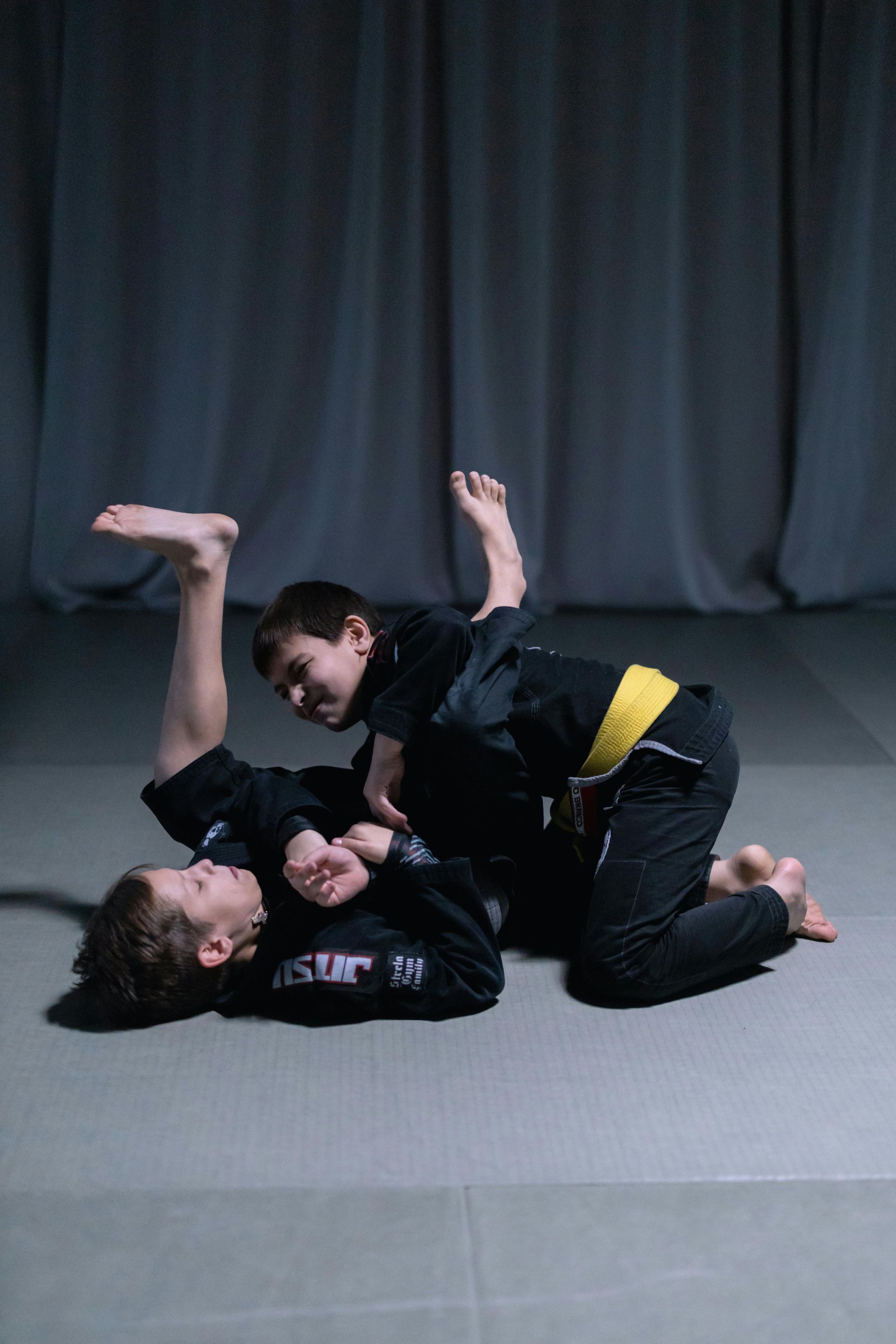 A man and a boy are wrestling on a mat in a gym.