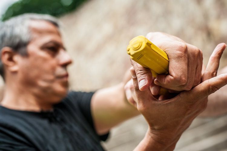 Man holding a yellow device in his right hand, possibly exercising or using for therapy, outdoors.