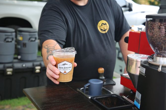 A man is holding a cup of coffee in front of a coffee grinder.